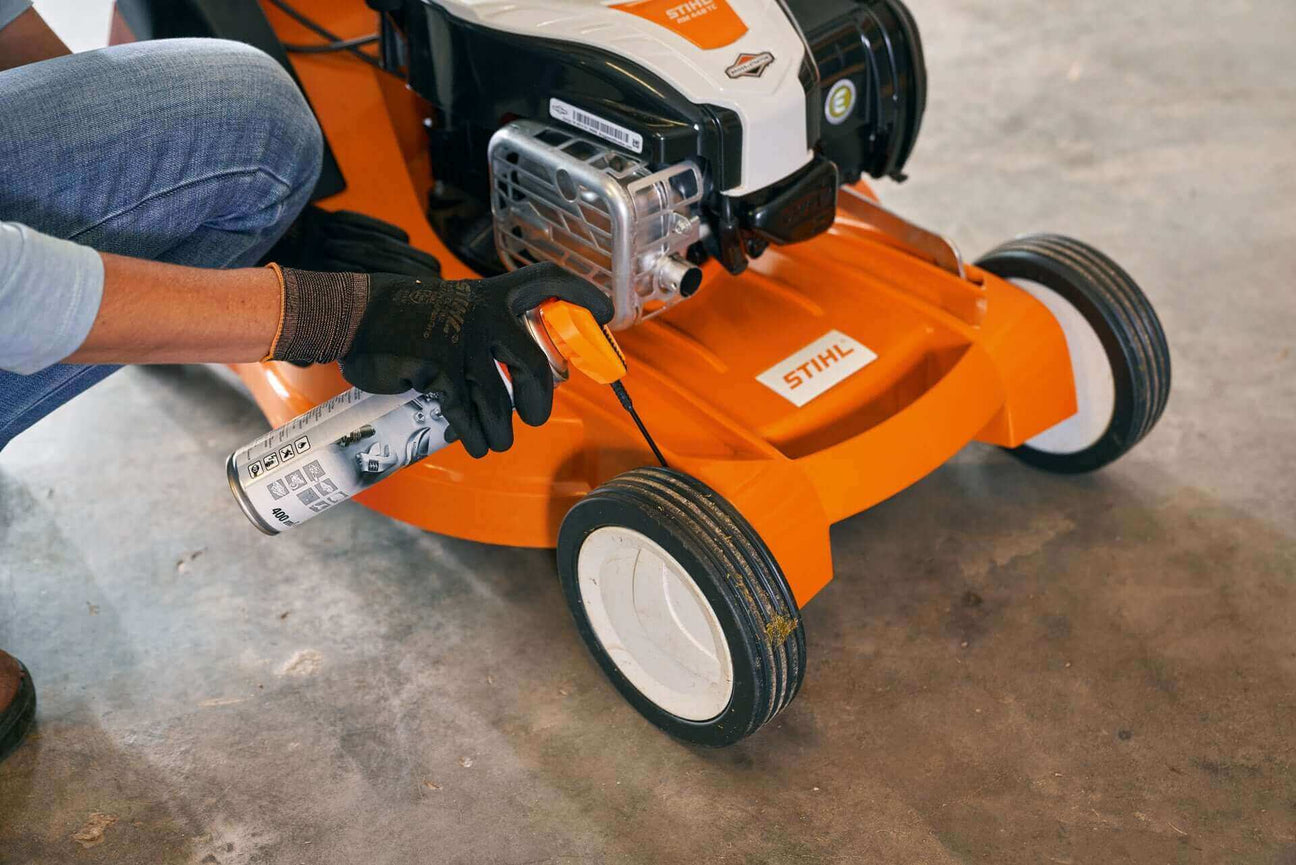 Person applying lubricant to a STIHL lawn mower tire for maintenance in a garage.