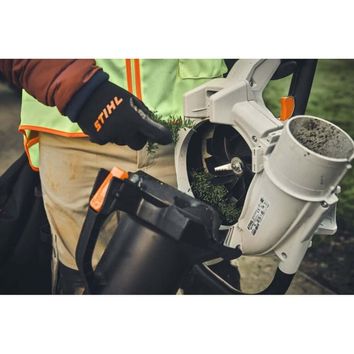 Tree surgeon using STIHL SHA 140 cordless leaf vacuum shredder with powerful suction for garden cleanup.
