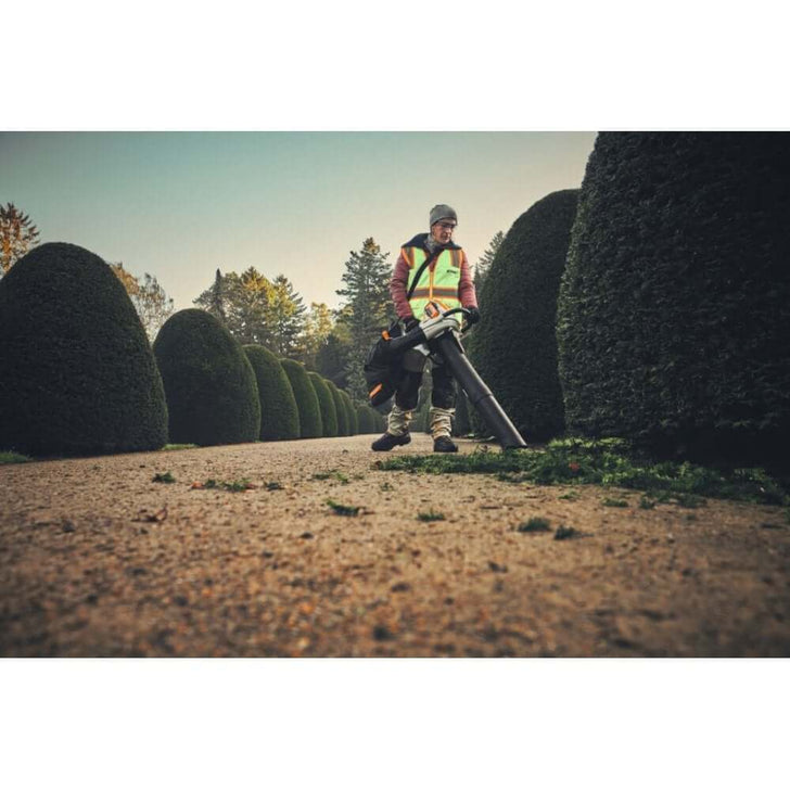 Tree surgeon using STIHL SHA 140 cordless leaf vacuum shredder in landscaped garden.