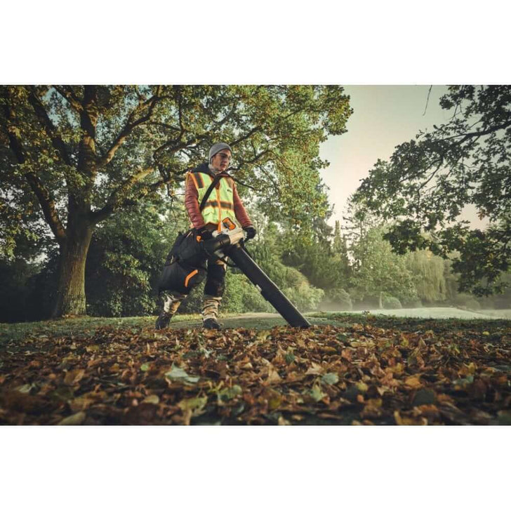 Tree surgeon using STIHL SHA 140 cordless leaf vacuum shredder in a leafy outdoor setting.