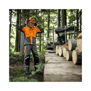 Tree surgeon wearing STIHL Function ERGO chainsaw trousers in forest, preparing to work with logs.