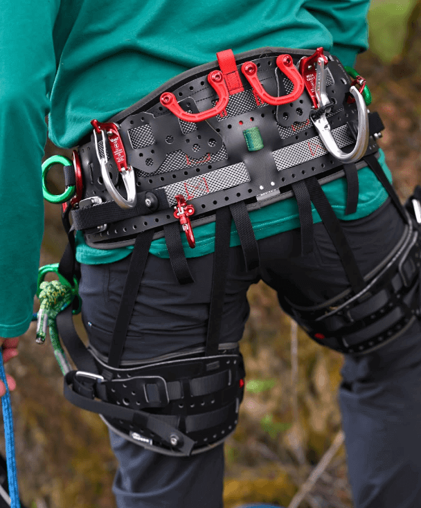 Climbing harness with carabiners and gear loops, worn by a climber outdoors, showcasing safety equipment.