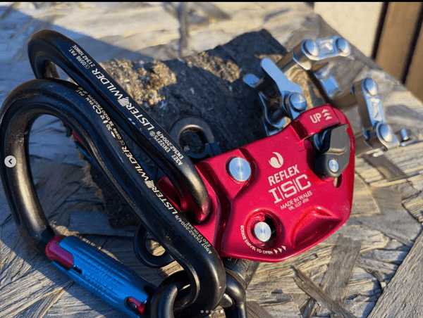 Close-up of a Reflex ISC climbing device with carabiners, showcasing its design and functionality on a wooden surface.