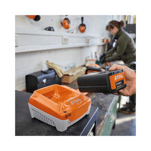 Stihl battery pack being charged on a workbench with a person in the background.