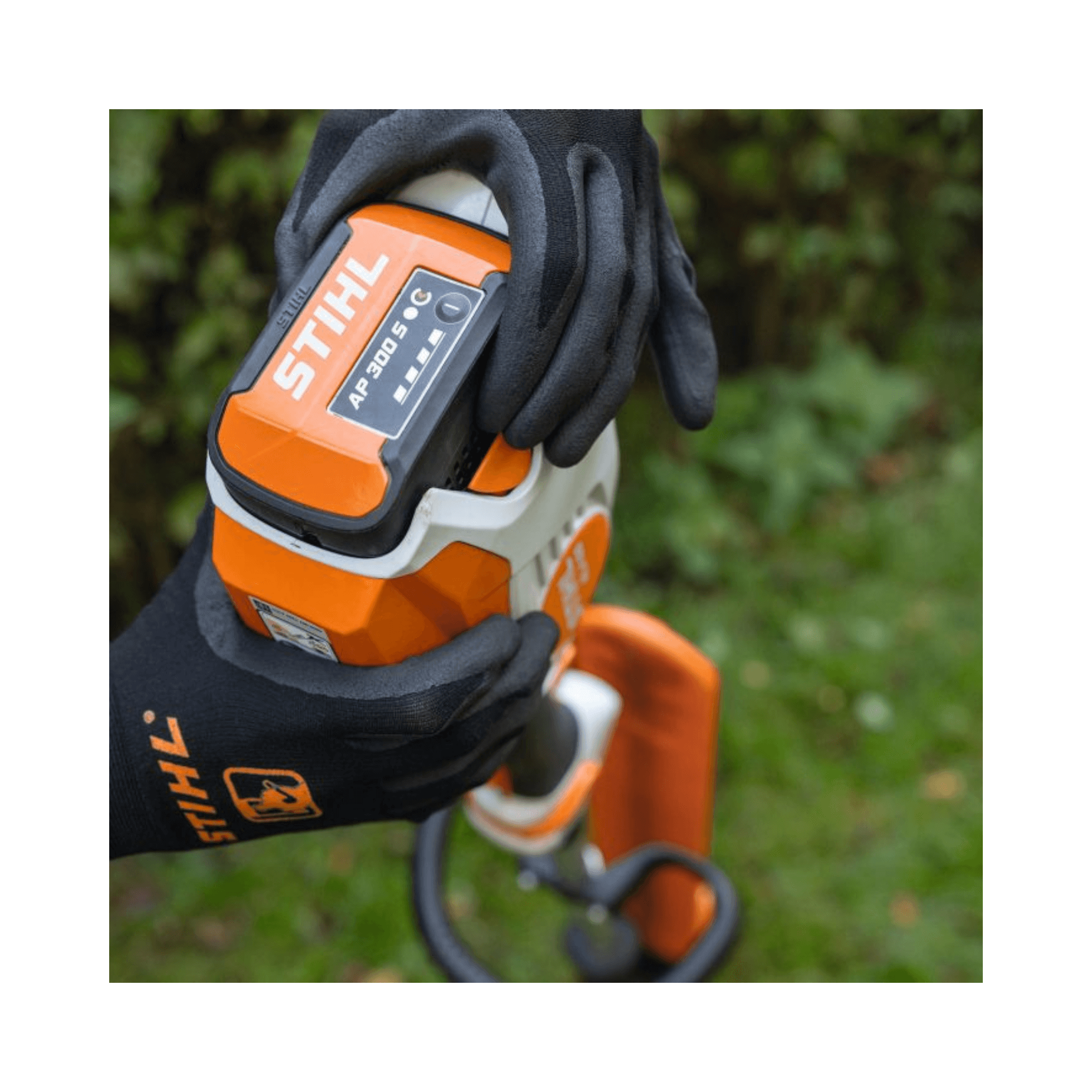 Stihl battery pack held by a gloved hand with a blurred green background