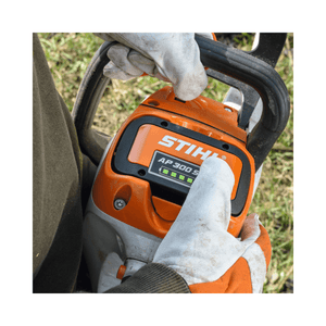 STIHL chainsaw being held by a person wearing gloves with a blurred natural background