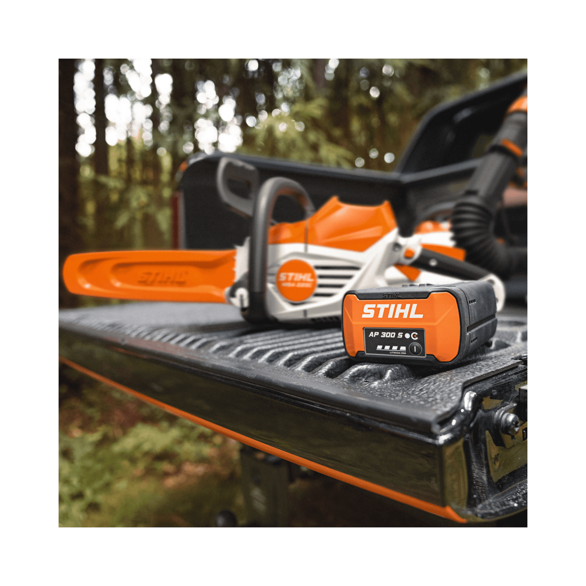 Stihl chainsaw and battery on a truck bed with a forest background