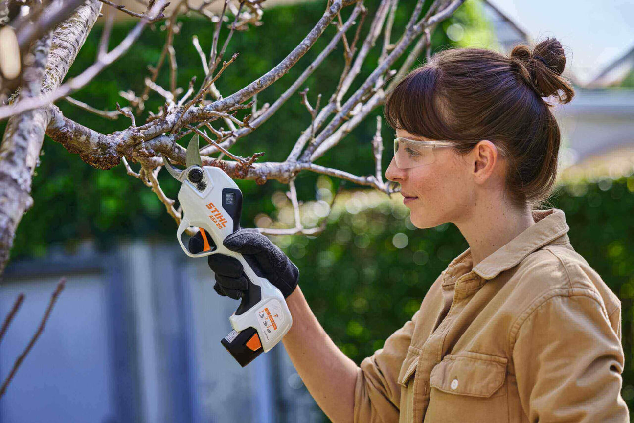 Tree surgeon using electric pruner to trim branches in a garden, demonstrating professional tree care techniques.