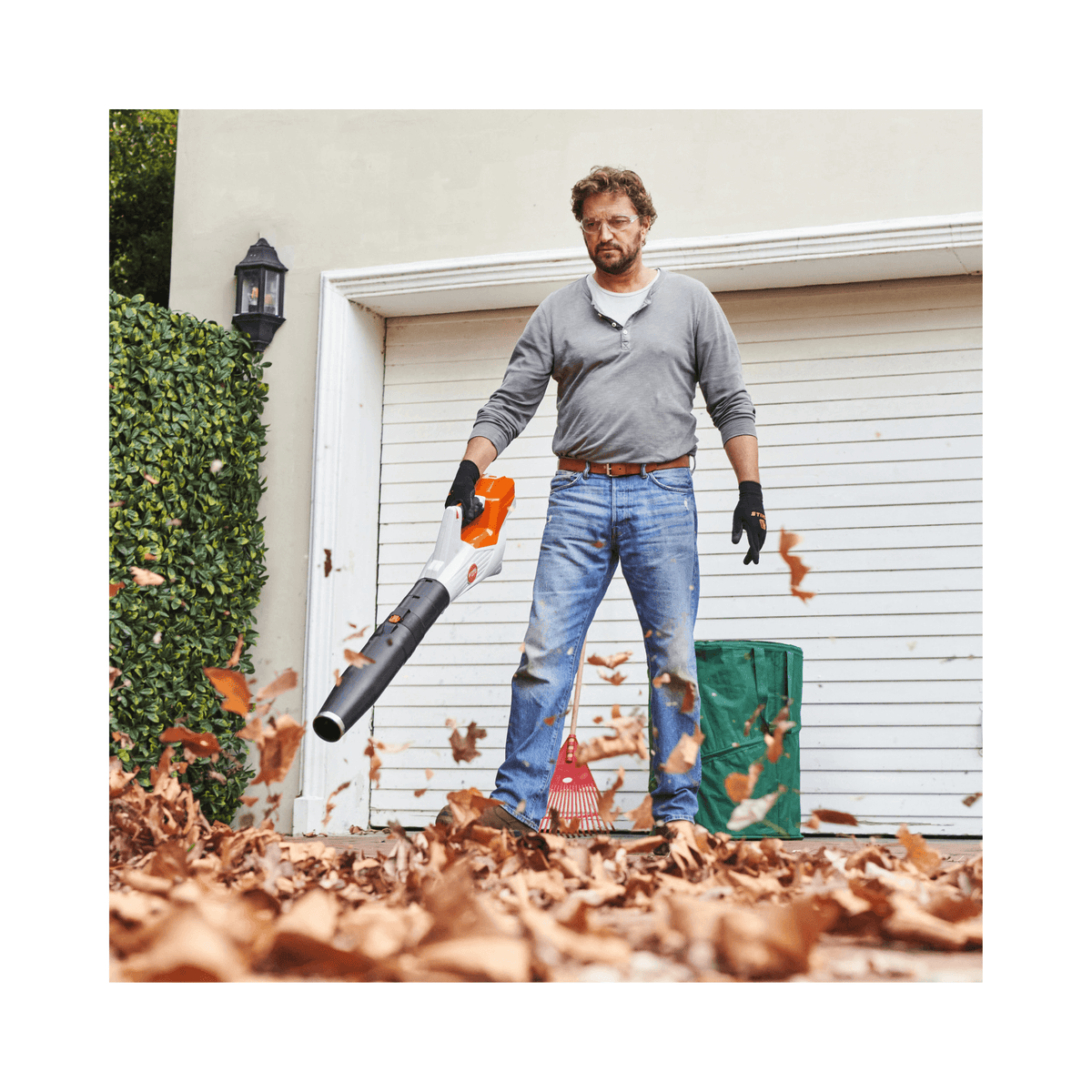 Person using BGA 60 Cordless Leaf Blower to clear leaves in a yard