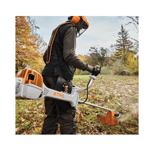 Person using a STIHL brush cutter in an outdoor setting with trees and grass.