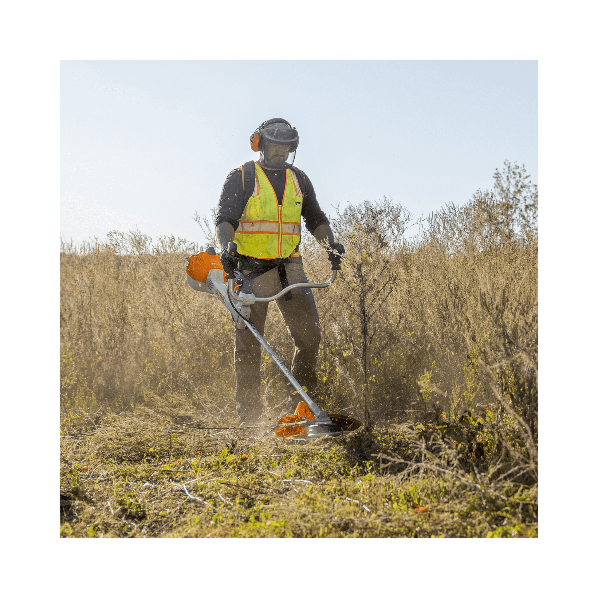 Tree surgeon using FS 461 C-EM Petrol Clearing Saw to clear brush in a sunny field, wearing safety gear.