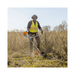 Tree surgeon using FS 461 C-EM Petrol Clearing Saw to clear brush in a sunny field, wearing safety gear.