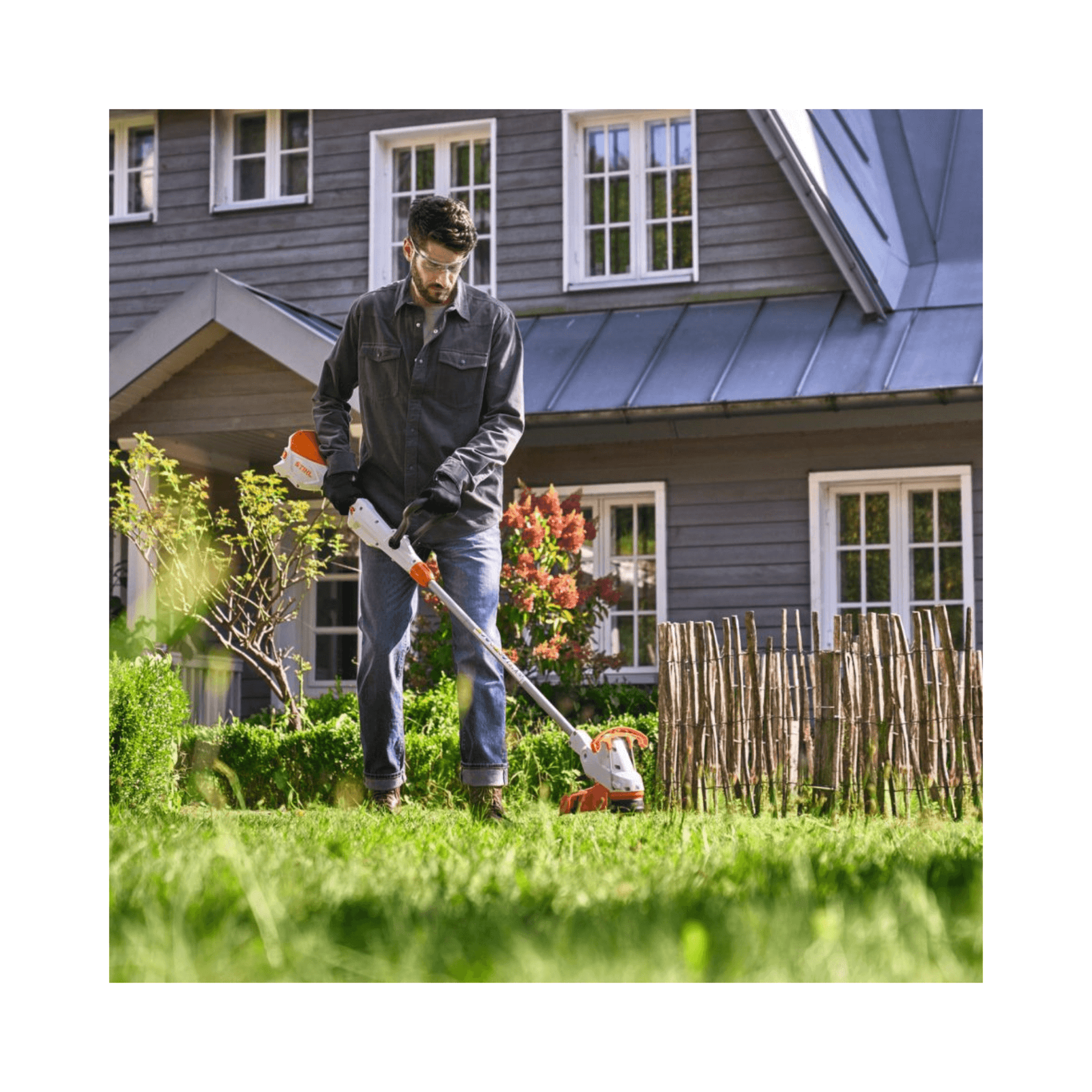 Man using a stihl grass strimemr in front of a house