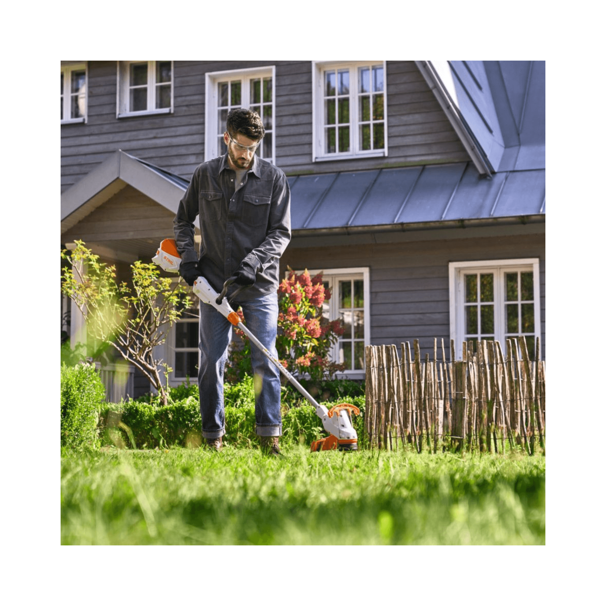 Man using a stihl grass strimemr in front of a house