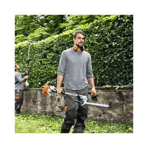 Man using HL 92 C-E Long Reach Petrol Hedge Trimmer for precise hedge shaping in a garden.