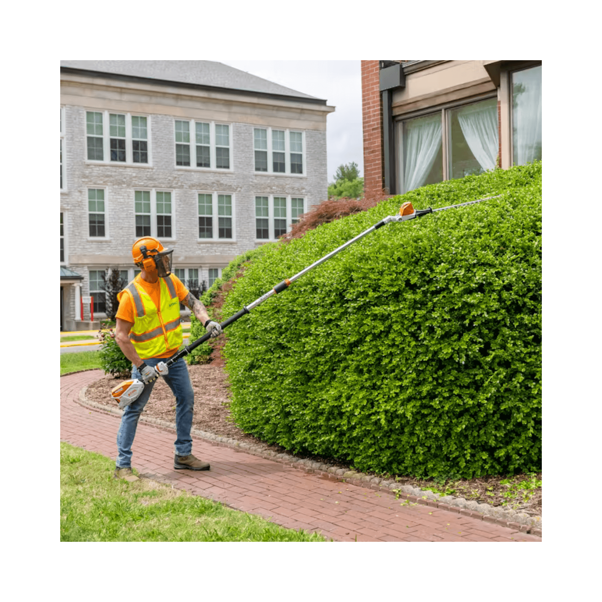 Person using a hedge trimmer to trim a bush in front of a house.