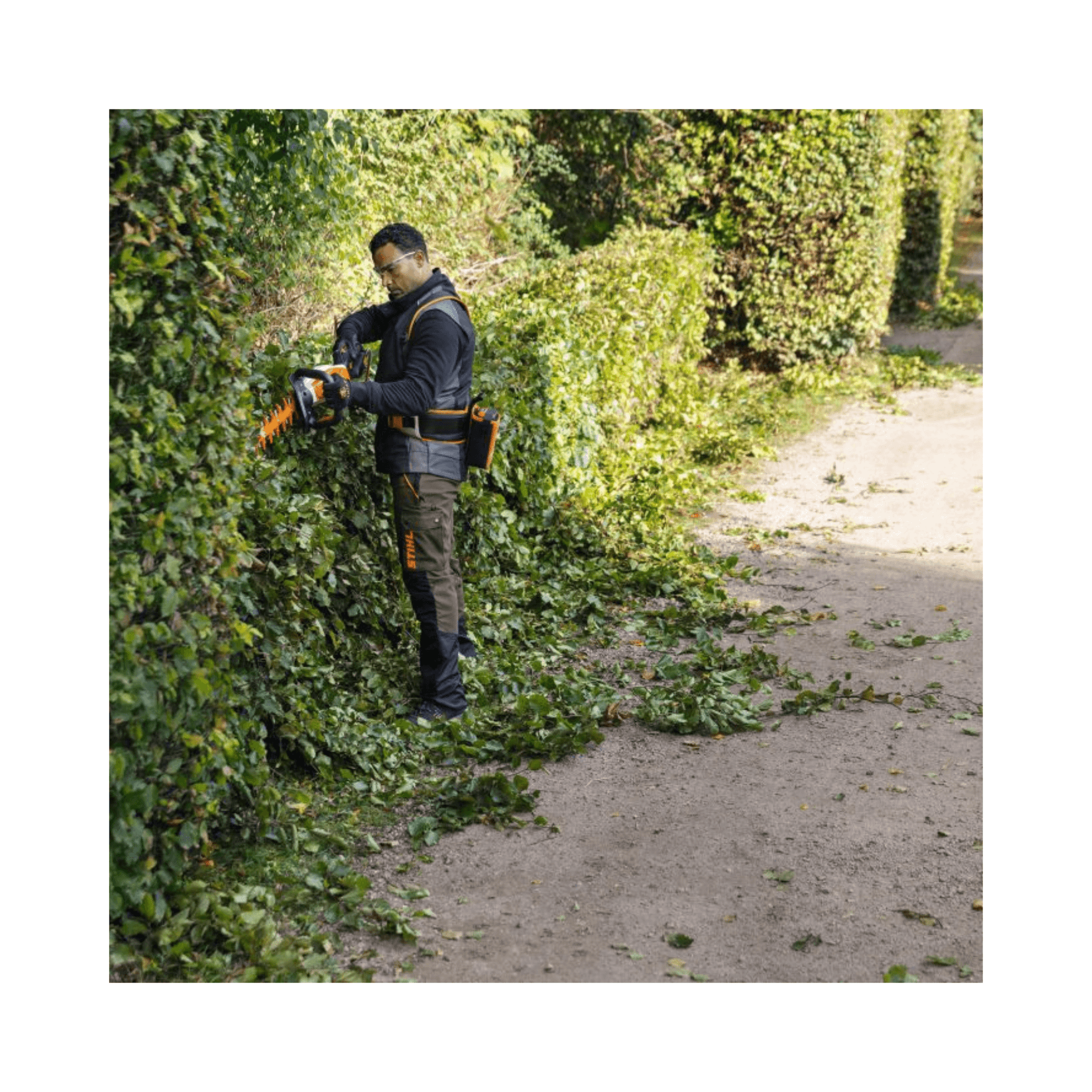 Professional using HSA 130 T Cordless Hedge Trimmer to shape hedges in a well-maintained garden.