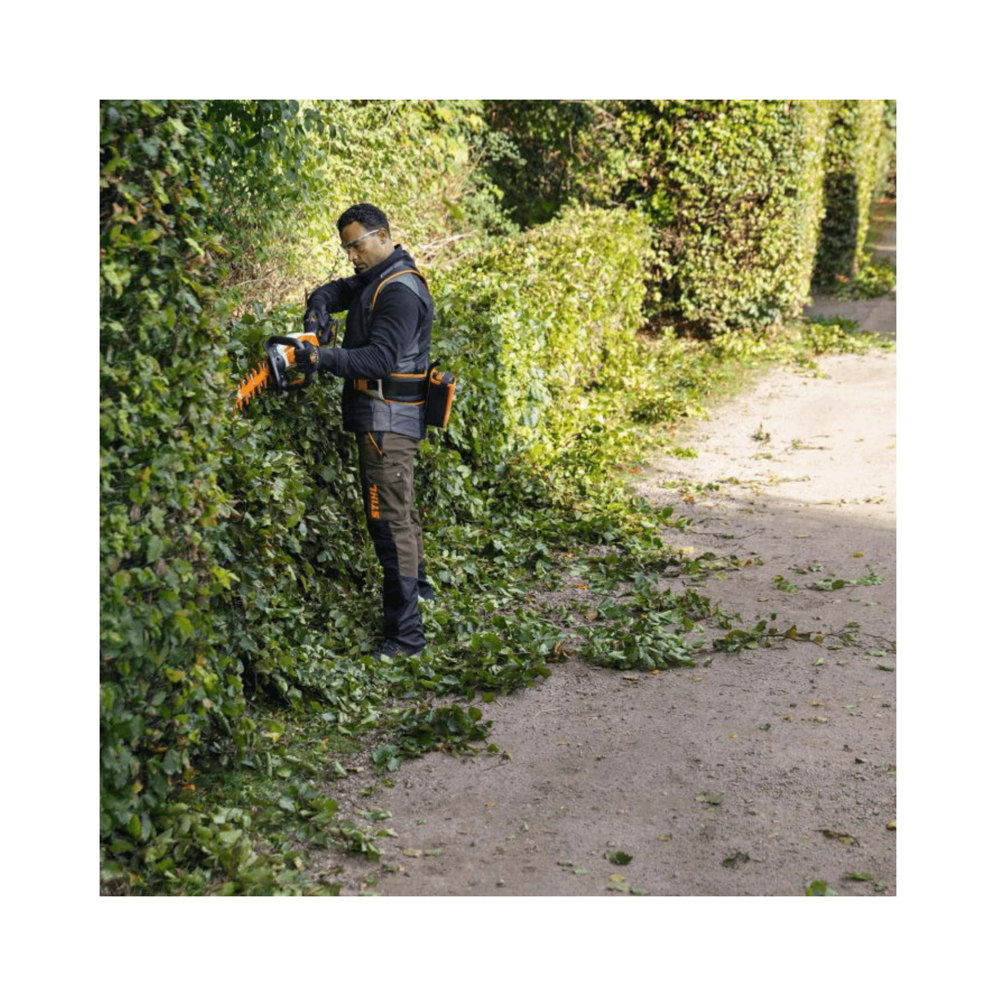 Professional using HSA 130 T Cordless Hedge Trimmer to shape hedges in a well-maintained garden.