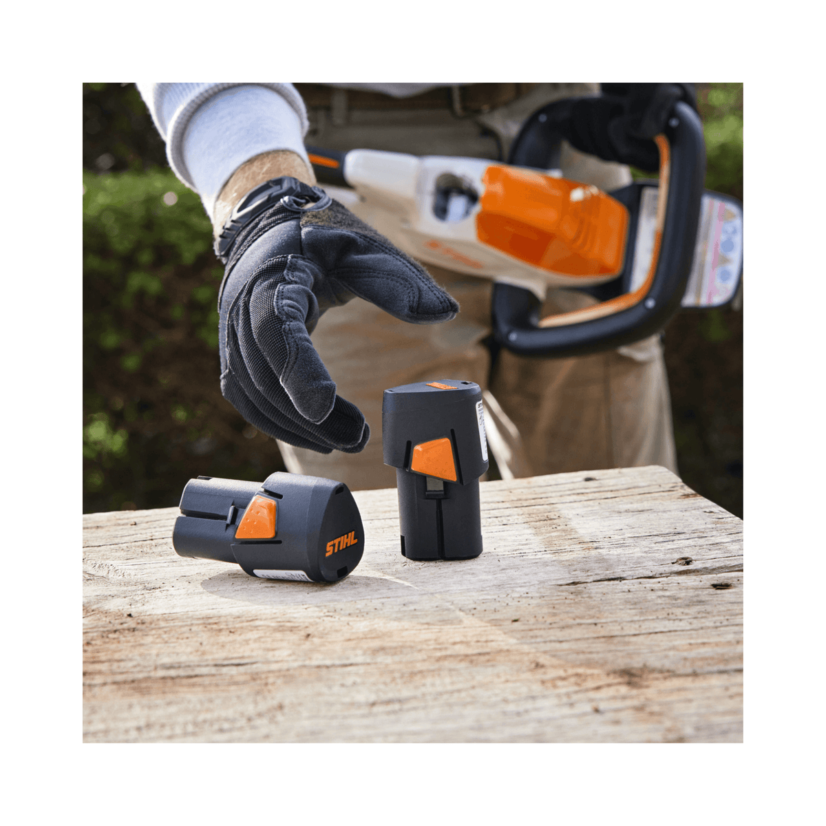 Two STIHL batteries on a wooden table, showcasing power source for HSA 40 Cordless Hedge Trimmer 20".