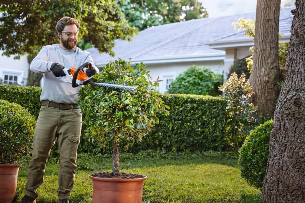 Man using HSA 40 cordless hedge trimmer to shape a small tree in a well-kept garden. Ideal for tree surgeons.