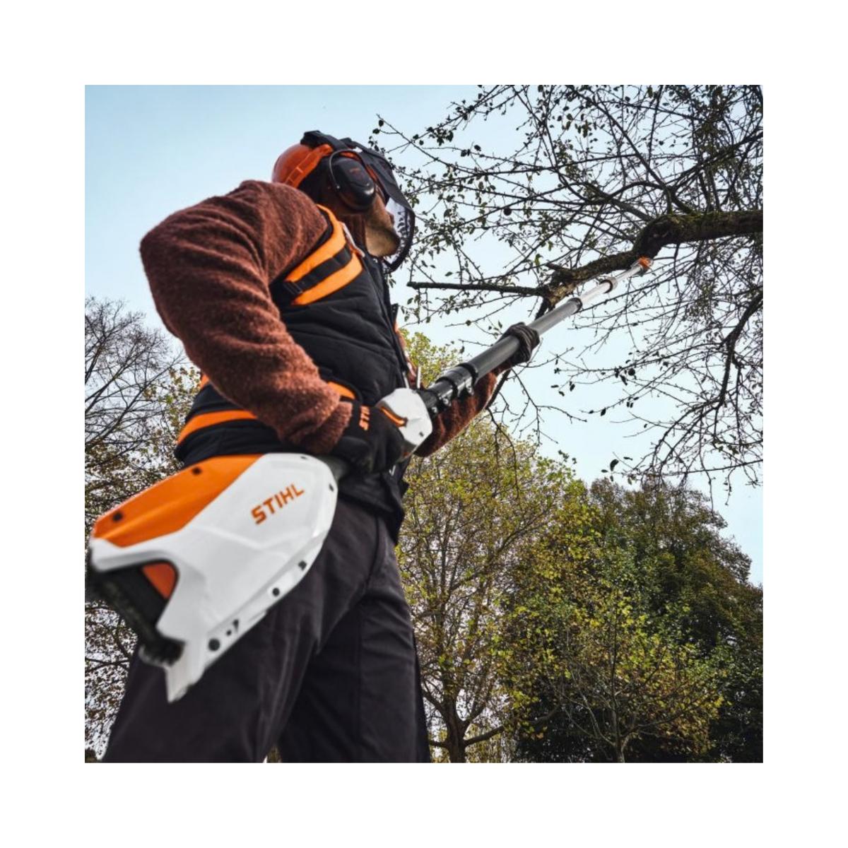 Man using HTA 110 Cordless Pole Pruner to cut tree branches outdoors with protective gear.