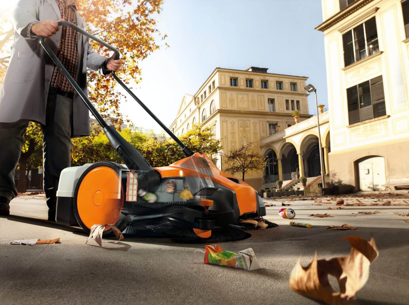Person using STIHL KGA 770 cordless sweeping machine to clean debris from a city sidewalk.