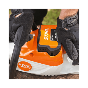 Close-up of STIHL MSA 70 C-B cordless chainsaw battery connection, showcasing gloves for safety and precision.