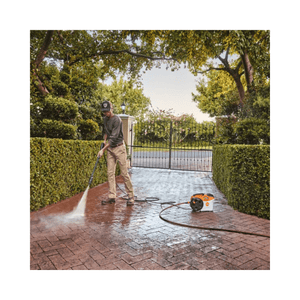 Person using REA 100 PLUS Cordless Pressure Washer on a brick driveway in a garden.