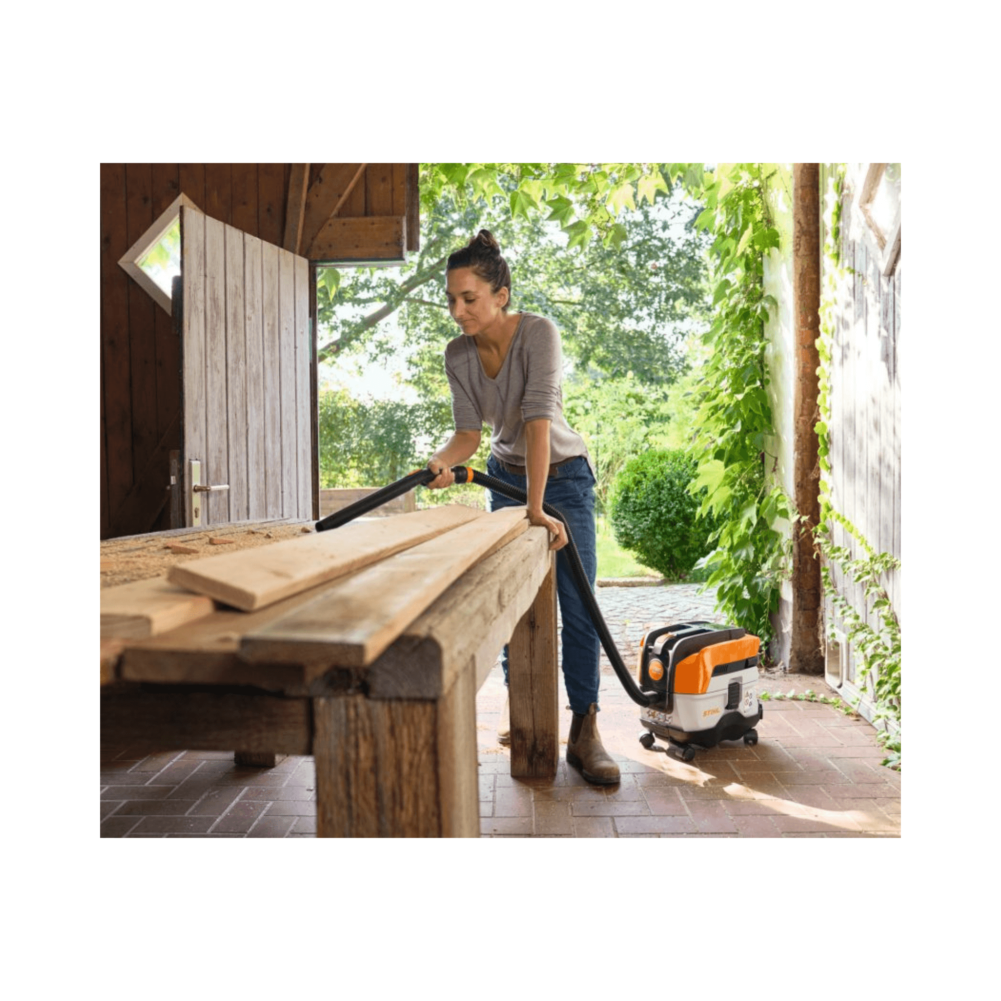 A woman using the STIHL SEA 50 Wheel Cart & Accessories with a vacuum cleaner on a wooden table outdoors.