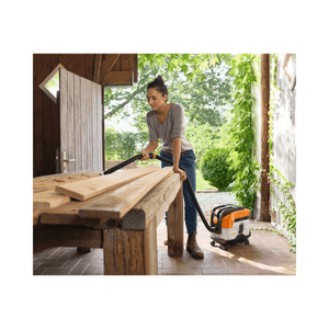 A woman using the STIHL SEA 50 Wheel Cart & Accessories with a vacuum cleaner on a wooden table outdoors.