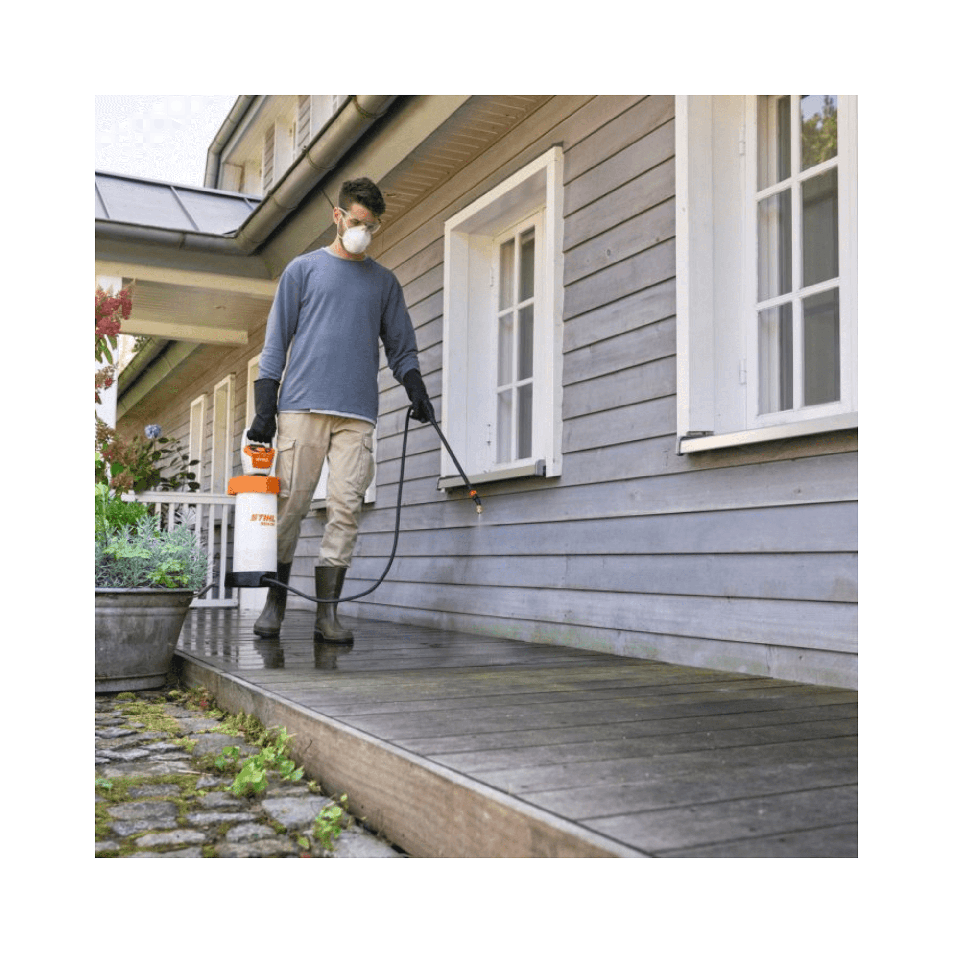 Man using SGA 30 Cordless Backpack Sprayer AS Battery Set on wooden deck near house.