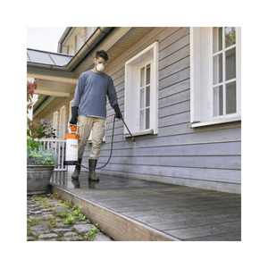 Man using SGA 30 Cordless Backpack Sprayer AS Battery Set on wooden deck near house.