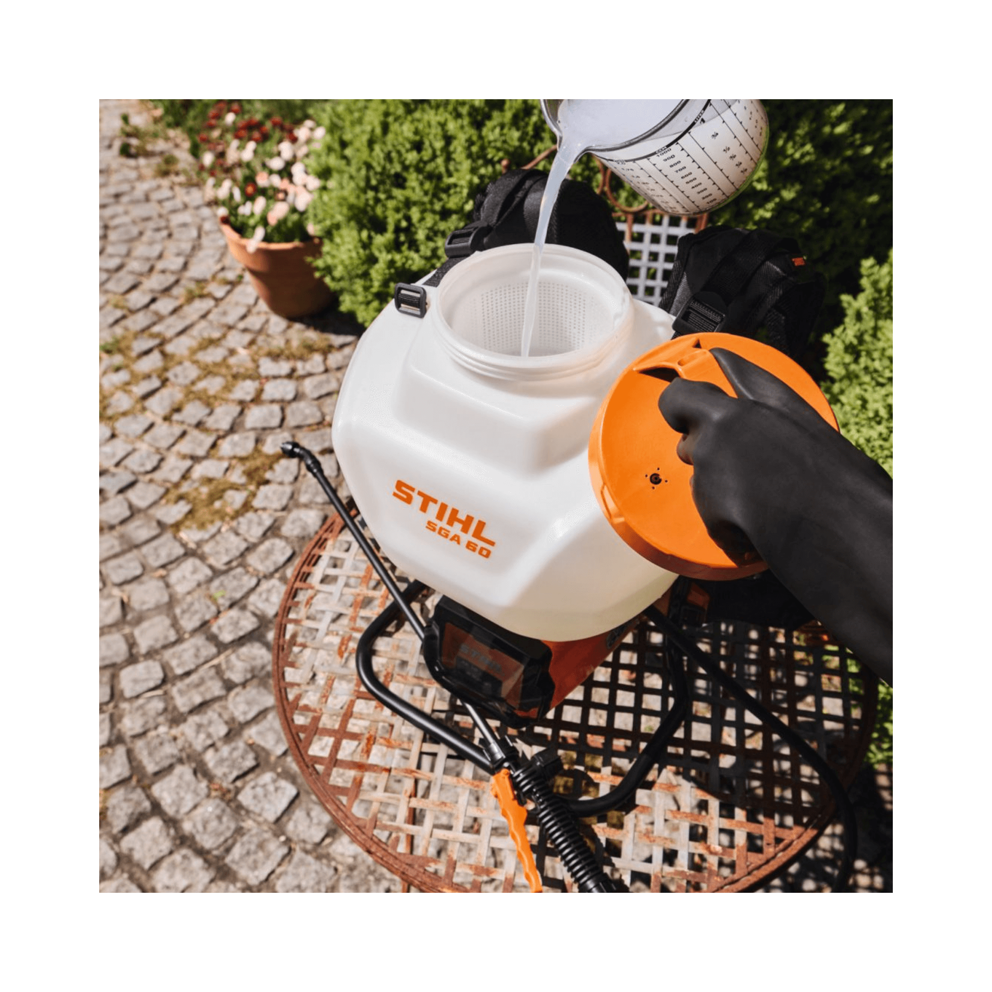 Filling the STIHL SGA 60 Cordless Sprayer with liquid on a sunny garden terrace.