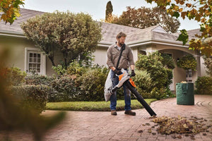 Person using the SHA 56 Cordless Leaf Vacuum Shredder in a landscaped garden.
