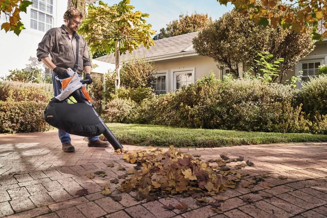 Person using SHA 56 Cordless Leaf Vacuum Shredder in a garden to clean up leaves.