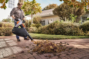Person using SHA 56 Cordless Leaf Vacuum Shredder in a garden to clean up leaves.
