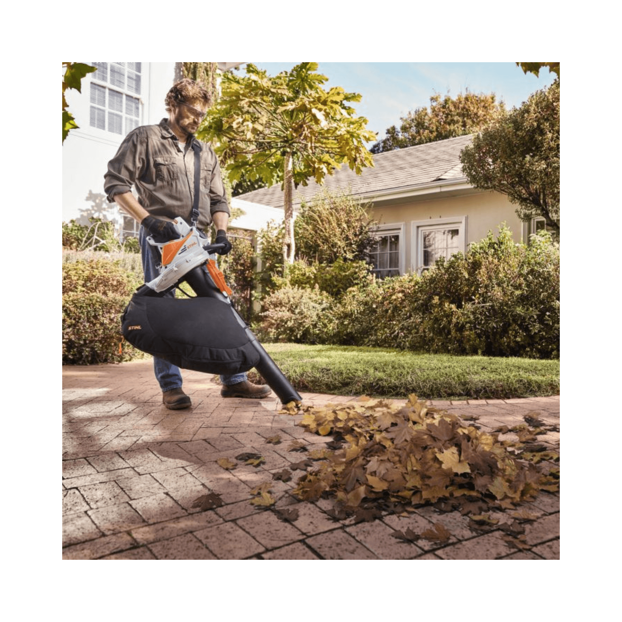 Man using STIHL SHA 56 Cordless Leaf Vacuum Shredder to clean up leaves in a garden.