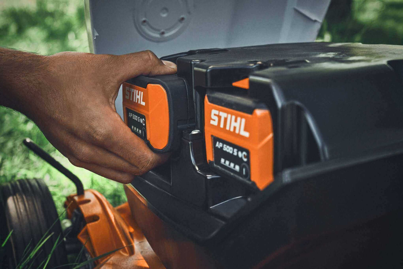 A hand installing a STIHL battery into a lawn mower, showcasing essential lawn care equipment in use.