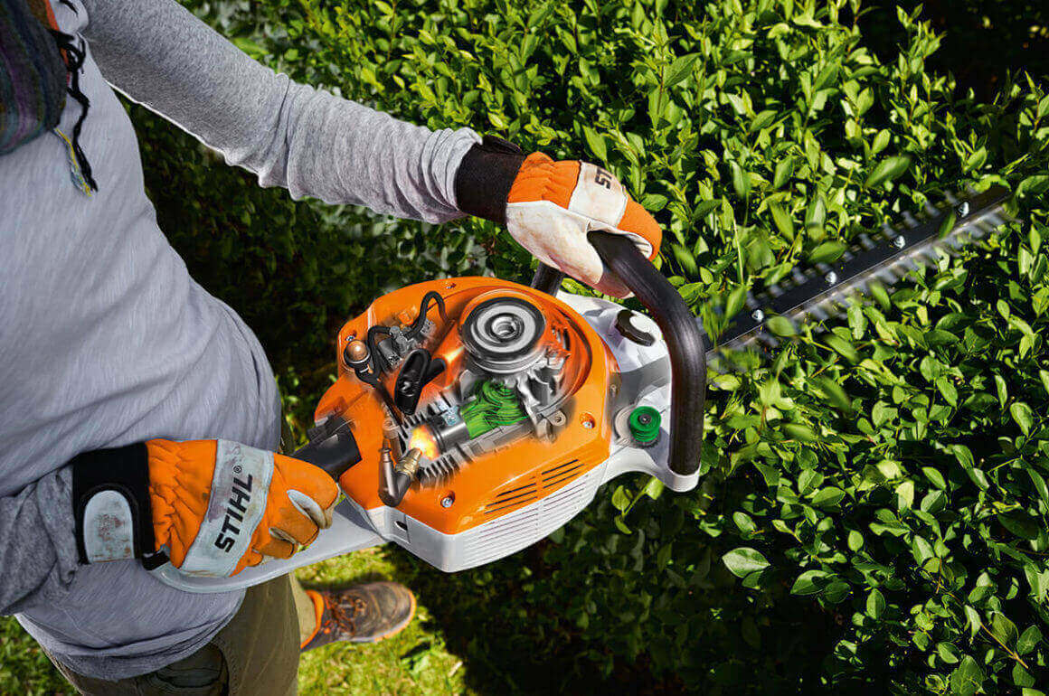 User using a STIHL hedge trimmer to maintain garden hedges, showcasing ergonomic design and power.