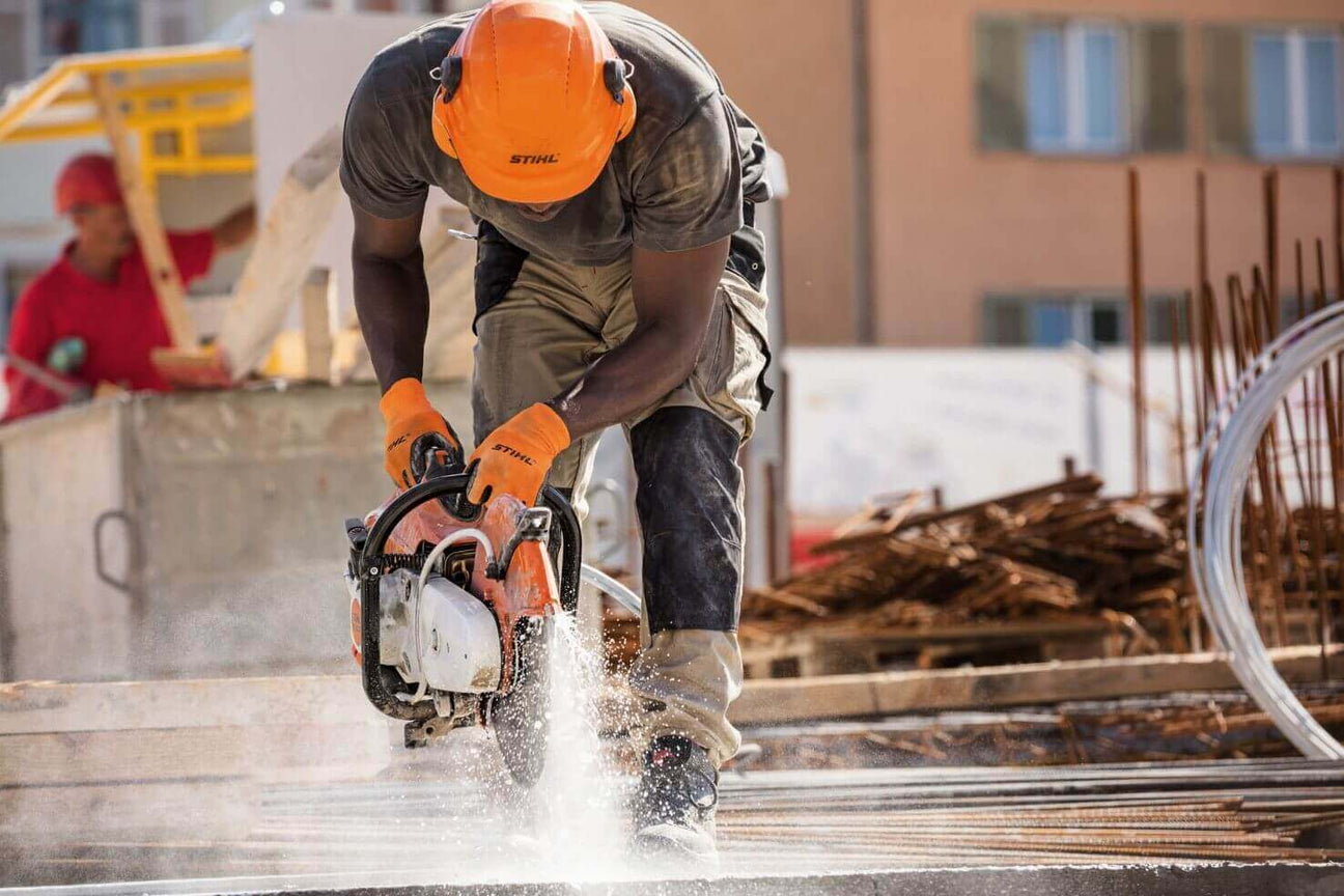 Construction worker using a concrete saw at a building site, with safety gear and dust in the air.