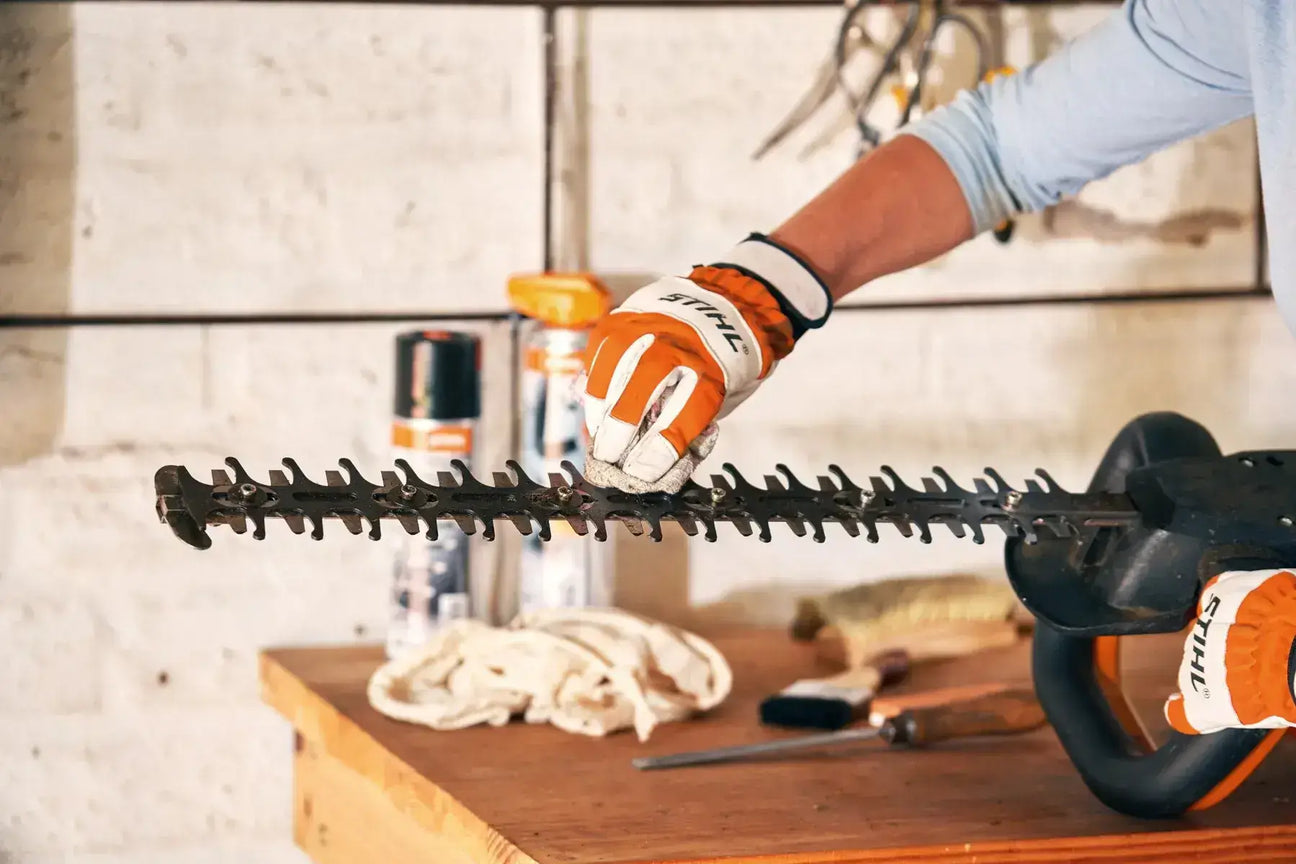 Close-up of a person using a hedge trimmer with safety gloves in a workshop.