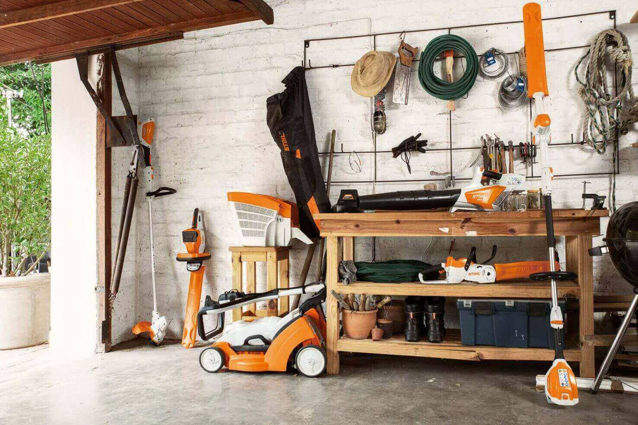 Well-equipped garage with garden tools, leaf blower, and lawn mower on wooden workbench.