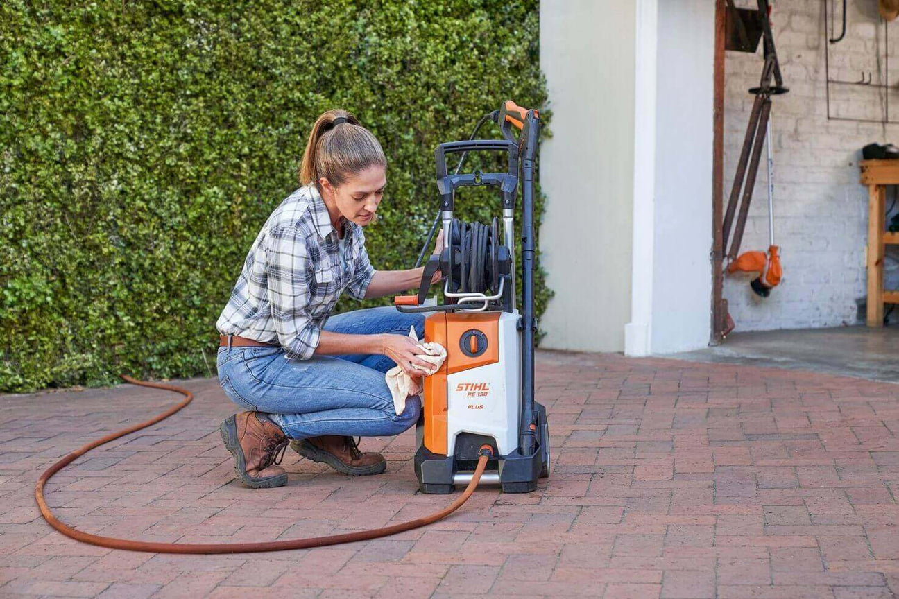 Woman cleaning a STIHL pressure washer in a driveway, showcasing outdoor maintenance tools.