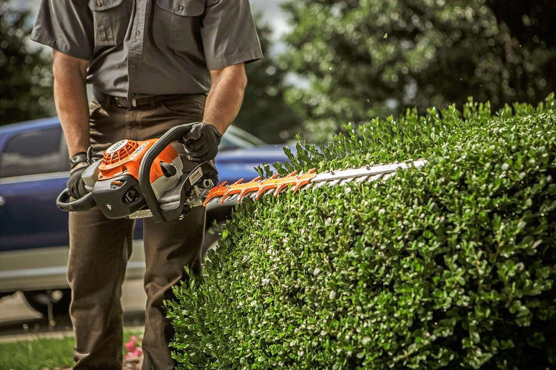 Person using a STIHL hedge trimmer to shape a lush green hedge outdoors.
