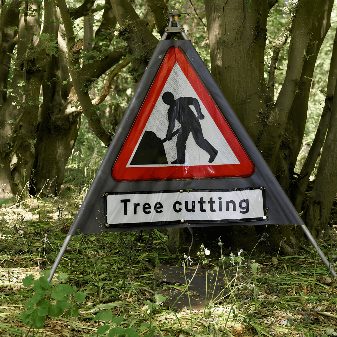 Caution sign for tree cutting in a forest, with worker silhouette and greenery in the background.