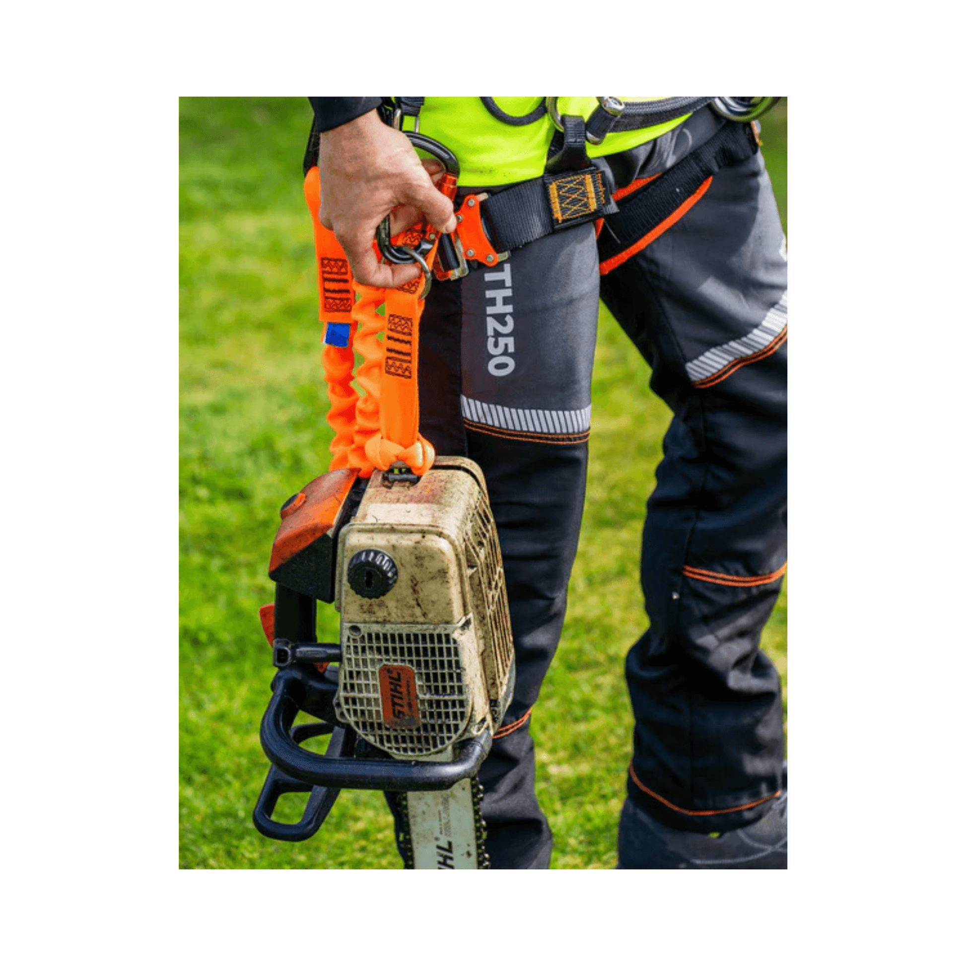 Person wearing Treehog TH250 Chainsaw Trousers holding a chainsaw outdoors, showcasing safety gear and tools for tree work.