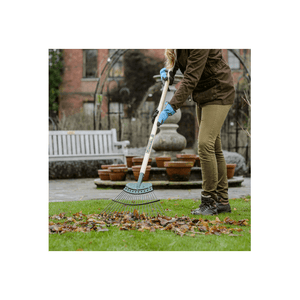 Person using a 20 tine Springbok lawn rake to clear leaves from a garden, showcasing durable gardening tools.