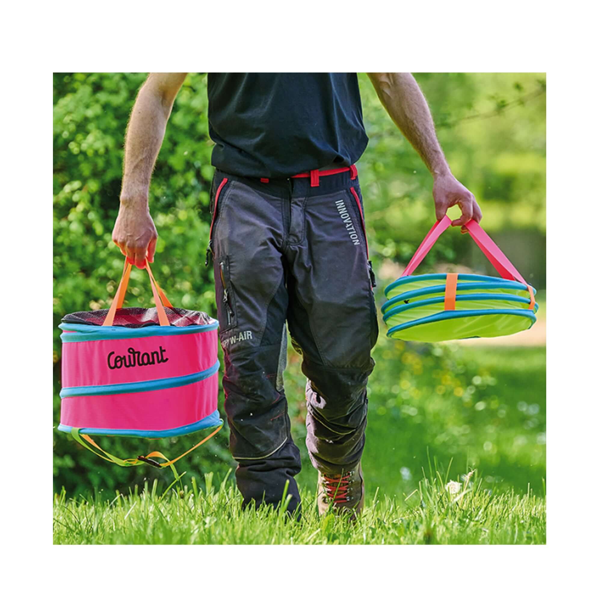 Person carrying two colorful Courant Pelican throwline bags for tree surgeons in a grassy area.