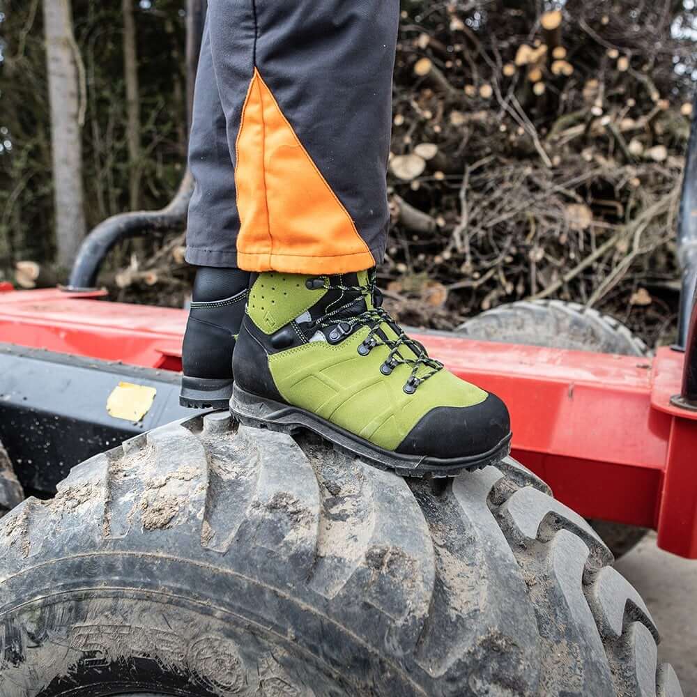 Person wearing Haix Protector Ultra 2.0 GTX chainsaw boots on a large tire in a forestry setting.