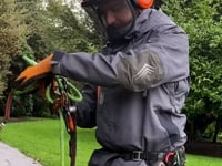 Tree surgeon wearing Harkie Defiance Smock Hi-Vis Orange, preparing equipment in a green outdoor setting.
